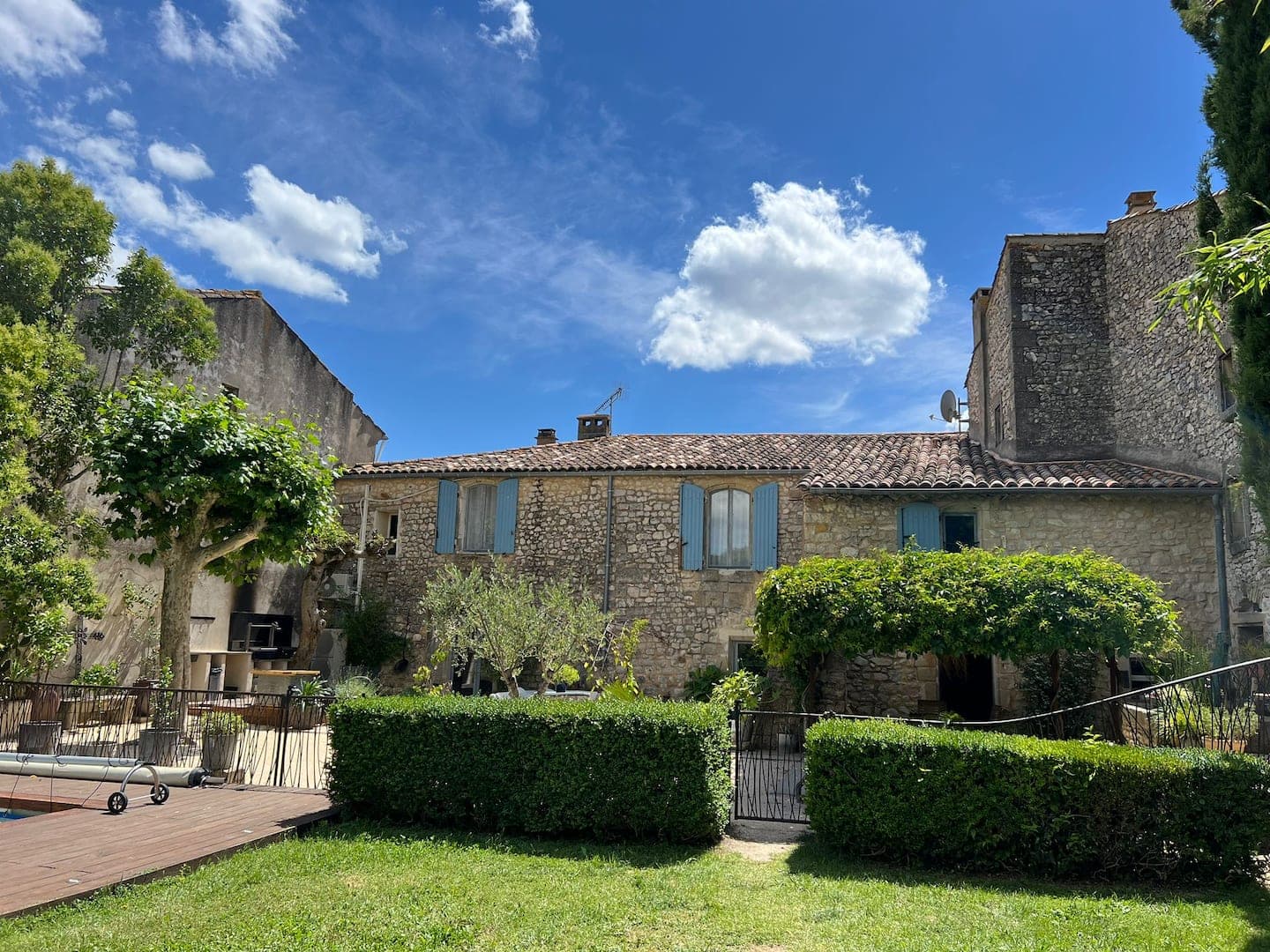 La façade en pierre vue du jardin, volets bleus et haies taillées