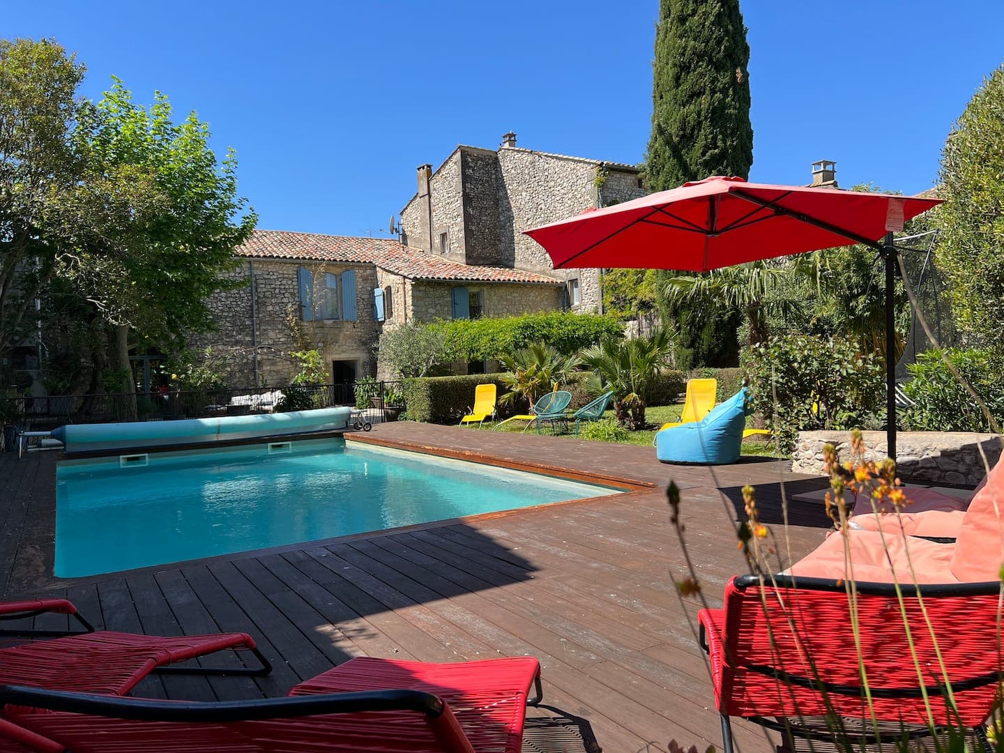 La piscine, la terrasse en bois et le parasol rouge