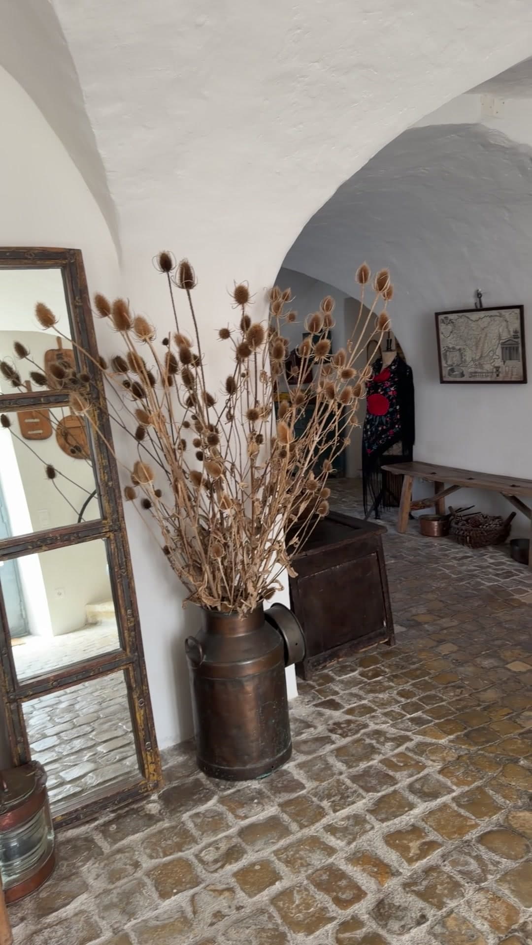 Cardères séchées dans un bidon de cuivre devant un miroir à cadre bois, enfilade vers la salle