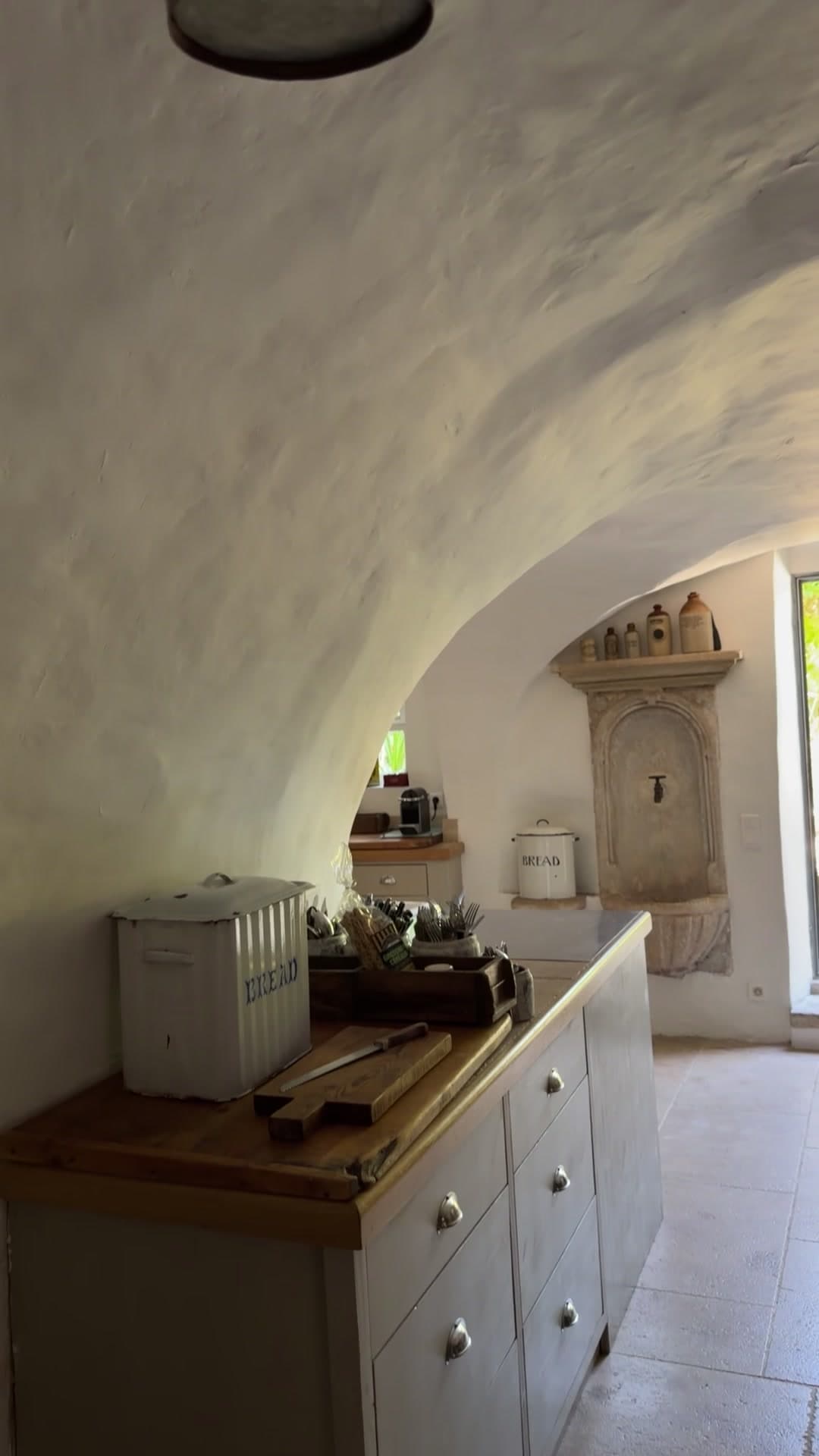 La cuisine sous voûte, son évier-fontaine en pierre et l'ouverture sur le jardin