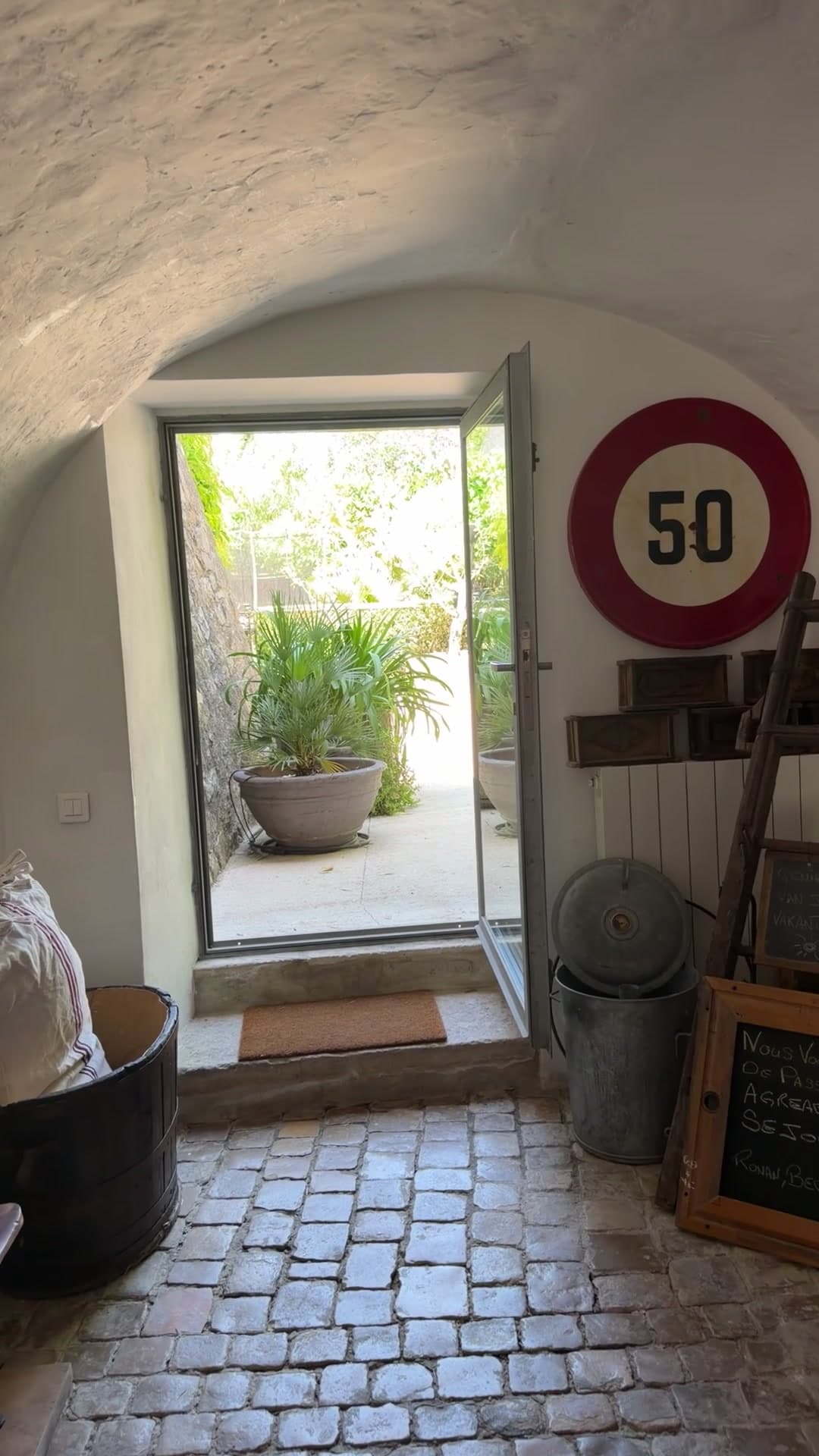 L'entrée voûtée et sa calade, porte ouverte sur la cour plantée, panneau 50 et ardoise au mur